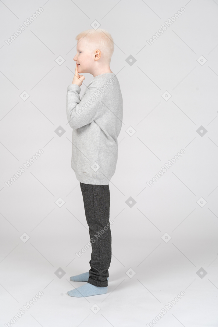 Vista lateral de um menino travesso, colocando o dedo nos lábios