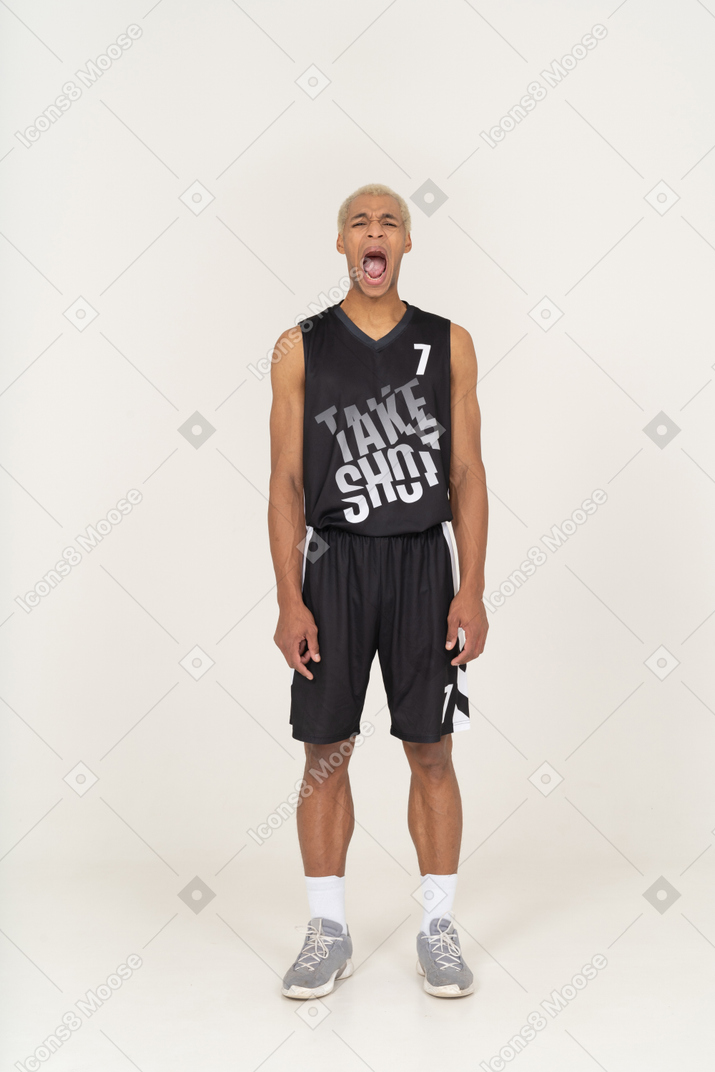 Vista frontal de un bostezo joven jugador de baloncesto de pie todavía
