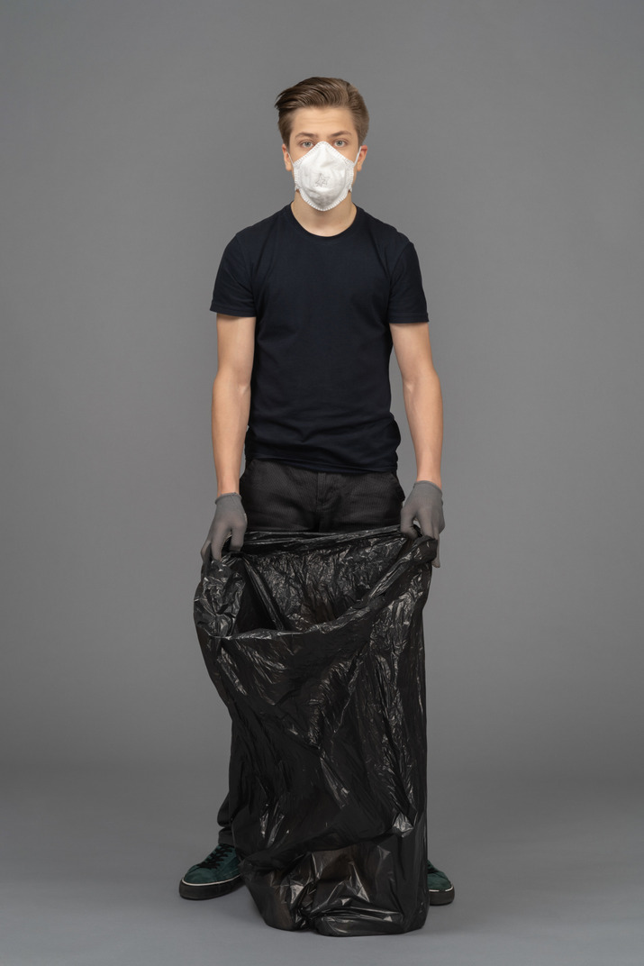 A young man wearing a mask while holding a trash bag