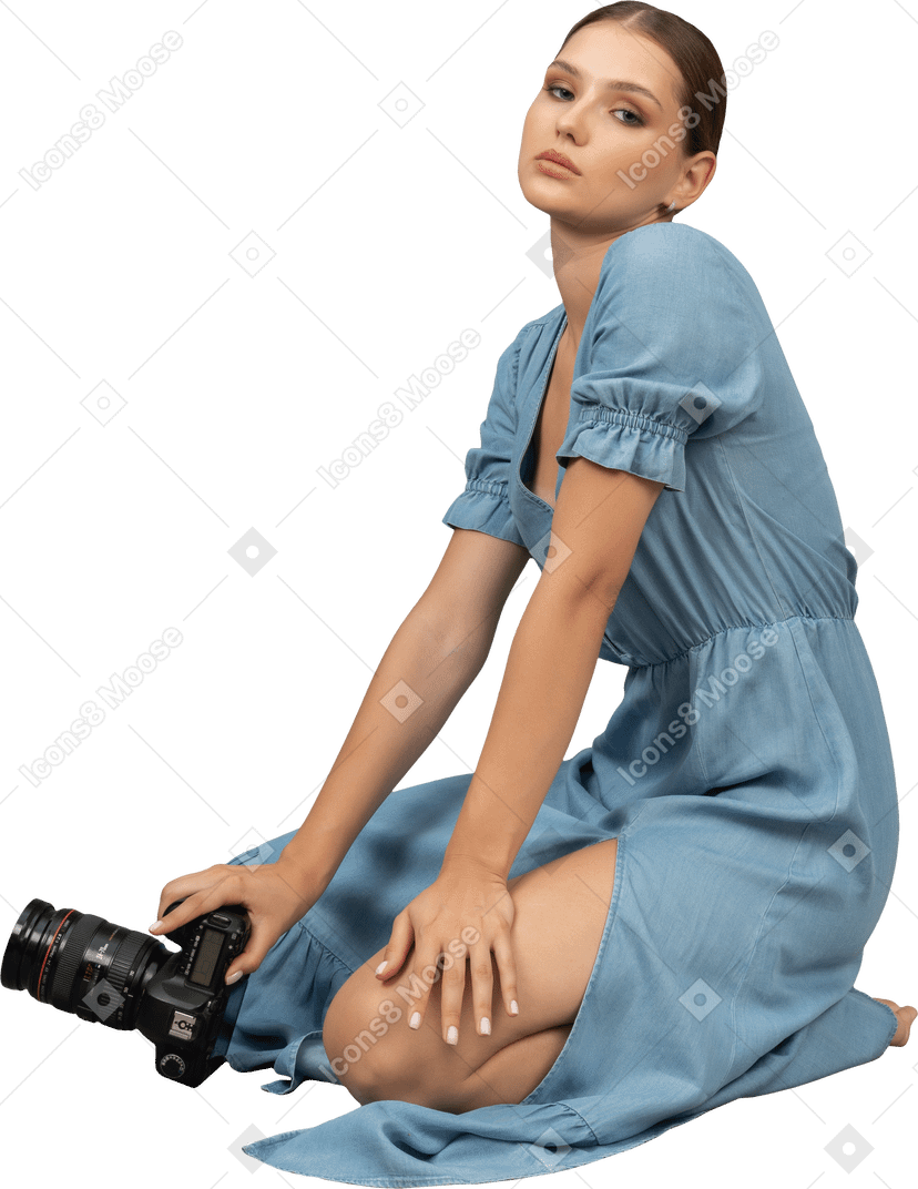 カメラと床に座っている青いドレスを着た若い女性の側面図
