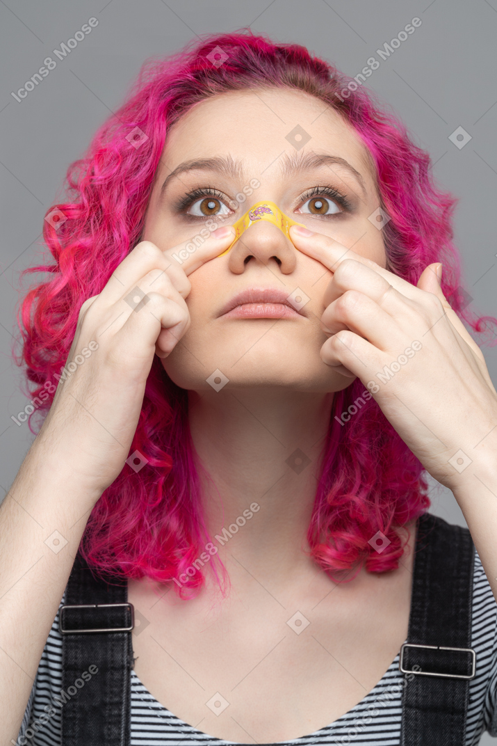 Teenage girl applying plaster on injured nose