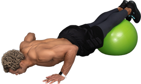 Three-quarter view of a shirtless afro man making push-ups on a gym ball