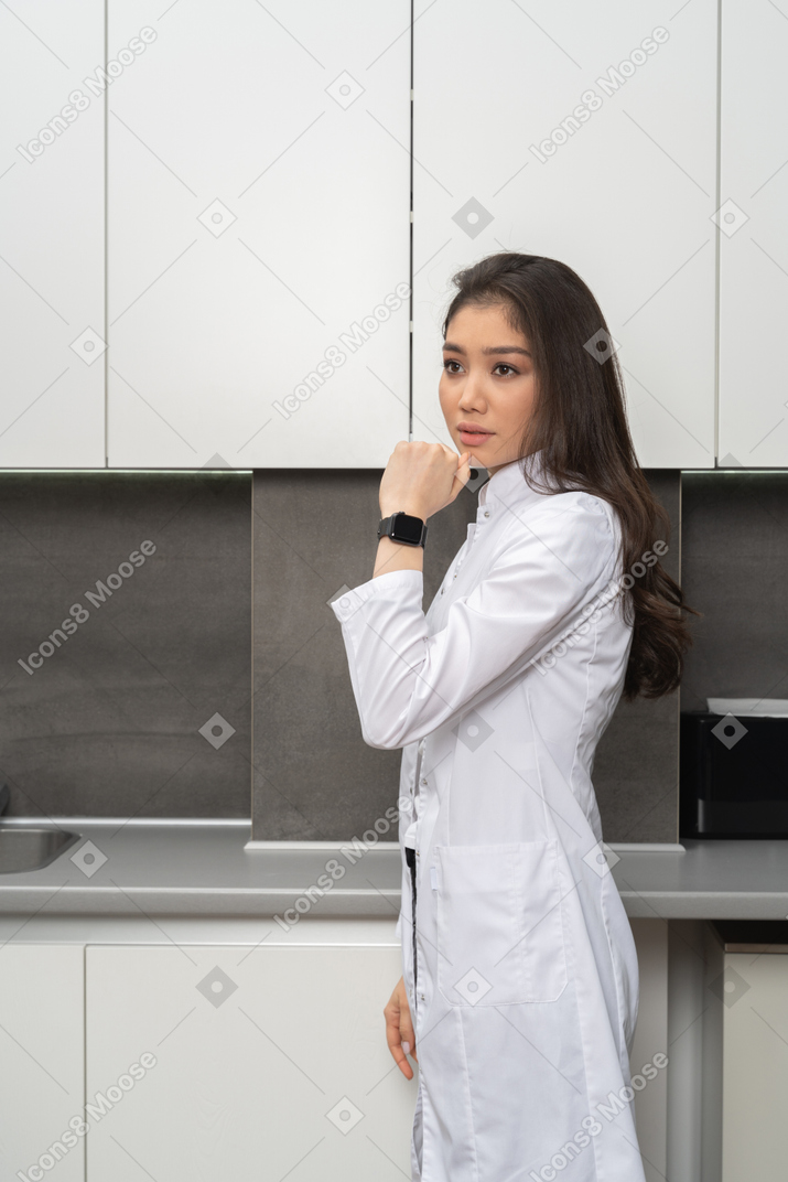 Vista lateral de uma mulher de jaleco branco mostrando seu smartwatch