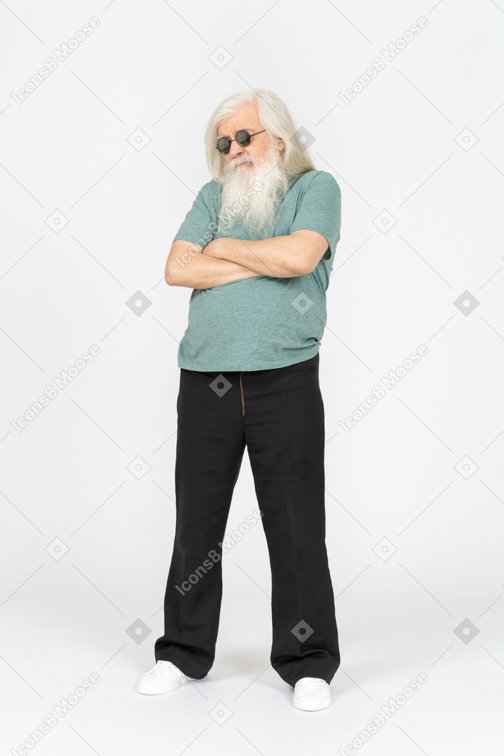 Vue de trois quarts du vieil homme à lunettes de soleil debout avec les bras croisés
