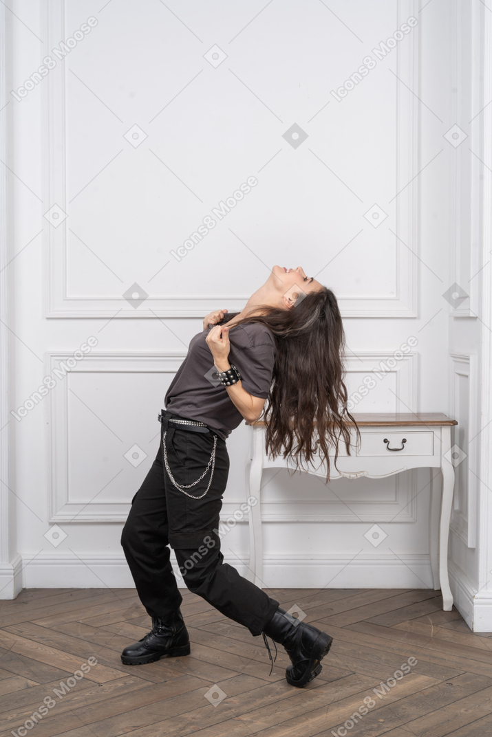 Vista lateral de una mujer rockera rasgando su camiseta mientras echa la cabeza hacia atrás