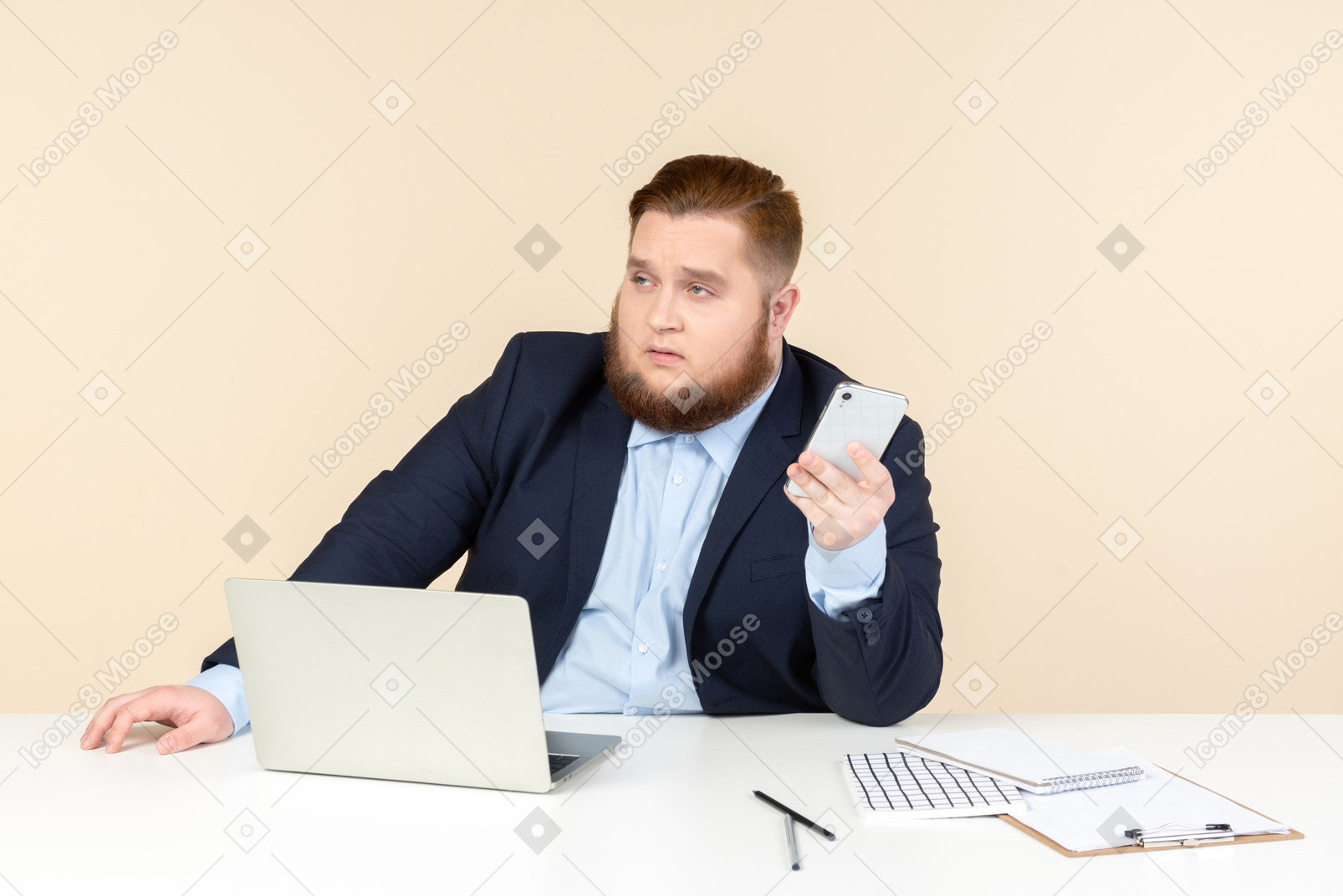 Pensive young overweight man sitting at the office desk and holding phone