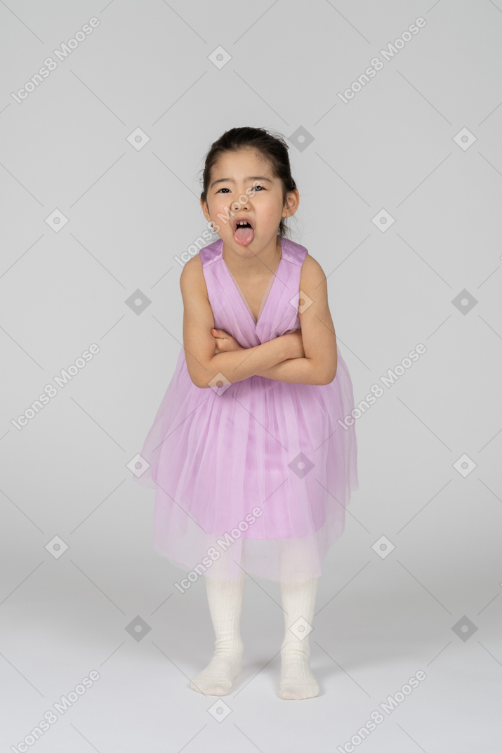 ピンクのドレスを着た少女が腕を組んで舌を出す