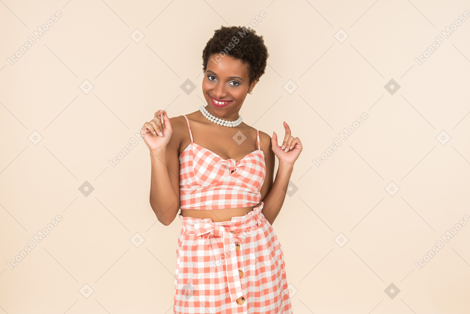 Jovem mulher de cabelo curto preto em um top xadrez e uma saia, posando contra um fundo peachy simples