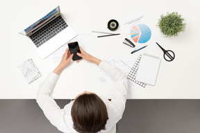 Une employée de bureau à la table tenant un téléphone portable