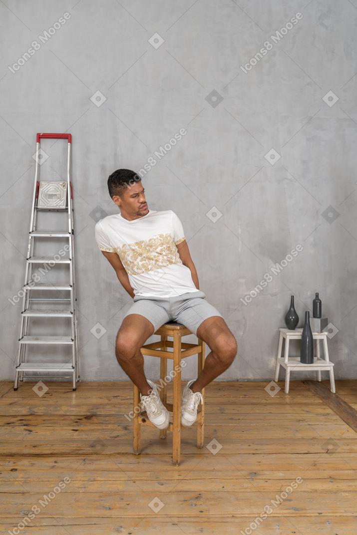 Young man sitting on stool and looking to the right