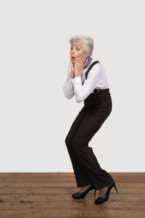 Three-quarter view of a surprised old lady in office clothing touching her face