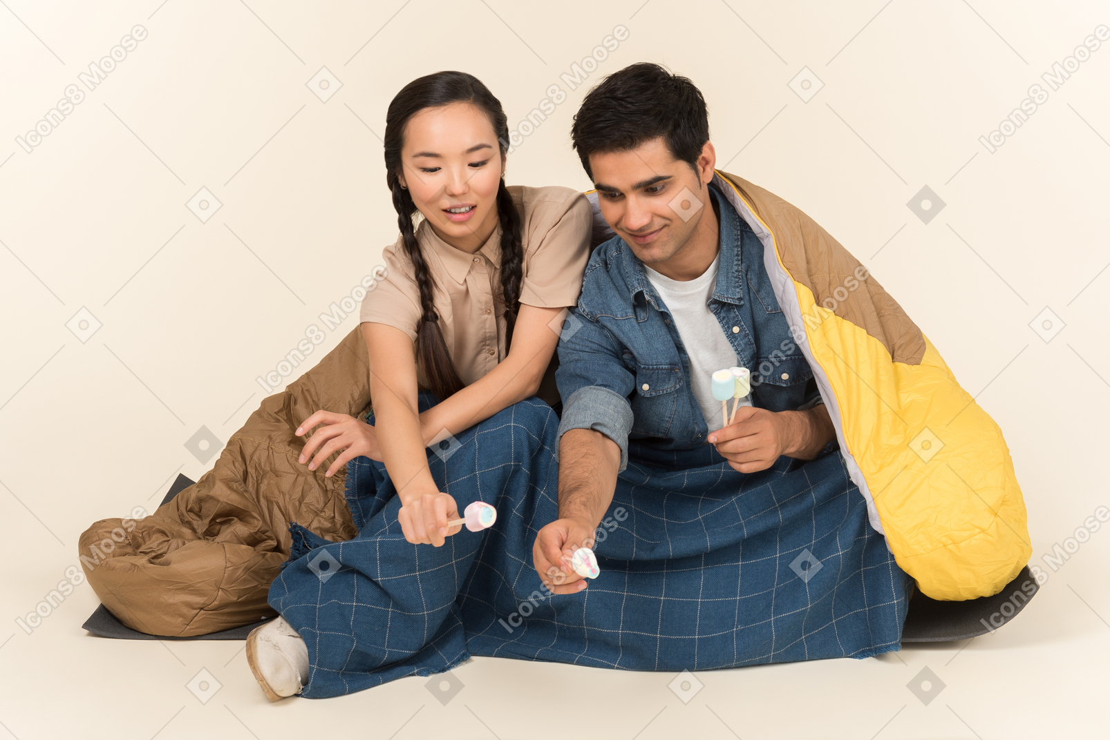 Jovem casal interracial sentado no saco de dormir e segurando marshmallows