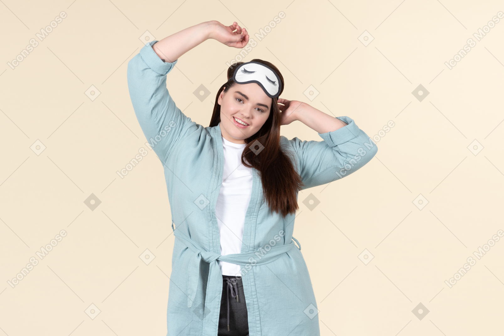 Young plus size woman in a blue bathrobe and a sleep mask on standing against a pastel yellow background, after just waking up