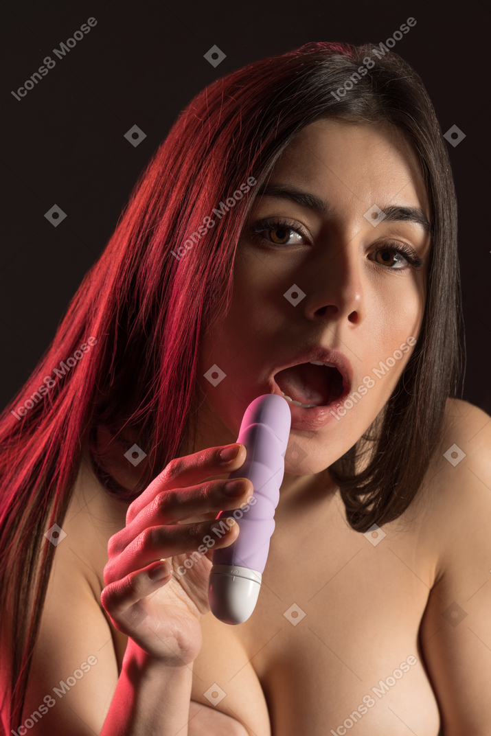 Close-up of sensual naked young woman holding a sex toy with mouth opened