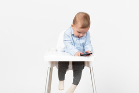 Baby boy sitting in highchair and using phone