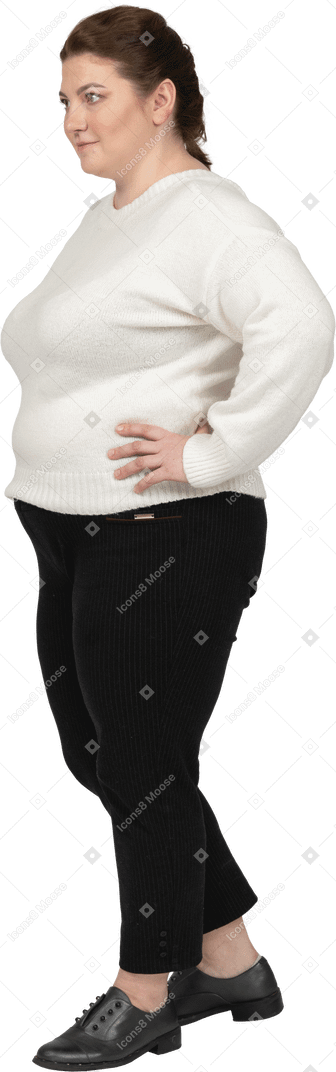 Пухлая женщина в белом свитере позирует, положив руки на бедра