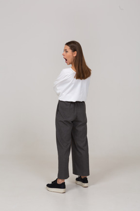 Three-quarter back view of a young lady in office clothing standing with mouth wide open
