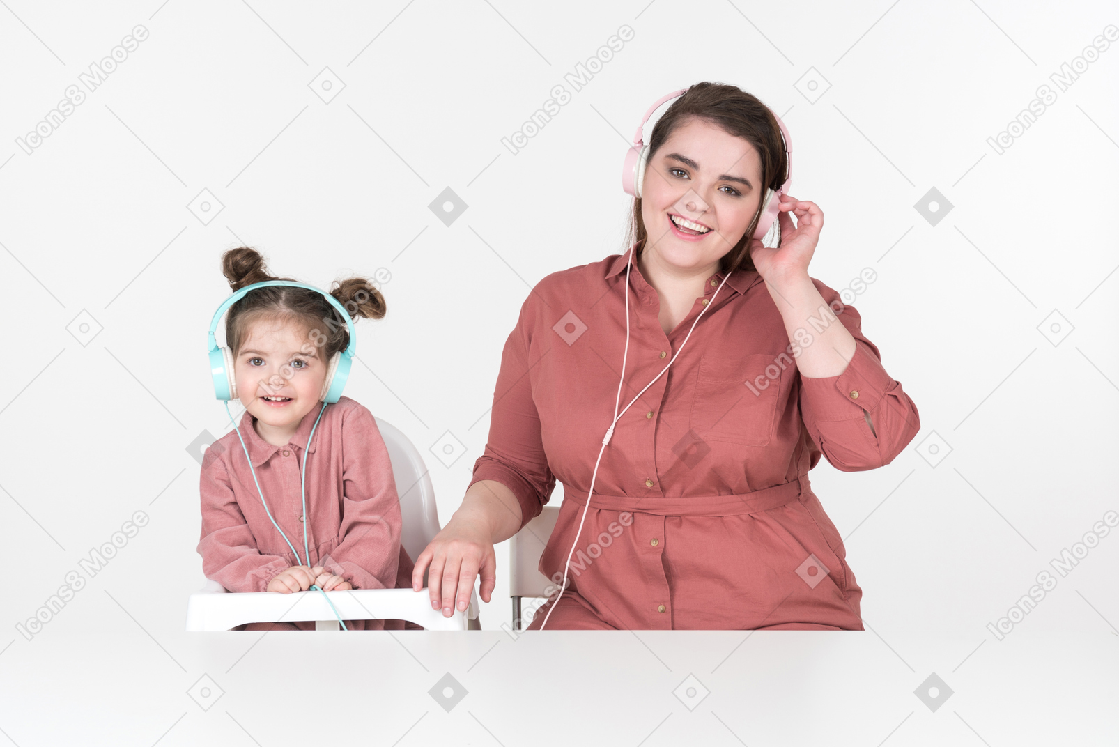 Madre y su pequeña hija, vestidas con ropas rojas y rosadas, sentadas a la mesa, escuchando la música juntas