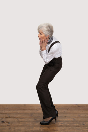 Side view of a surprised old lady in office clothing touching her face