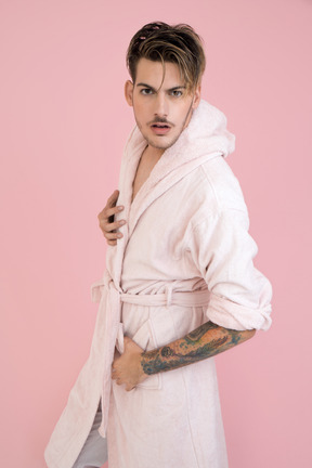 Handsome young guy standing in pink robe and watching to the camera closely