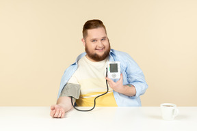 Sorrindo jovem homem com excesso de peso, verificação de pressão arterial