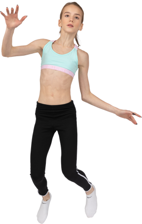 Вид спереди девушки-подростка в спортивной одежде, протягивающей руку во время прыжка