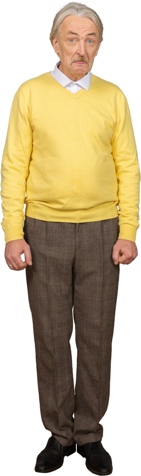 Vue de face d'un vieil homme dans un pull jaune montrant la langue et regardant la caméra