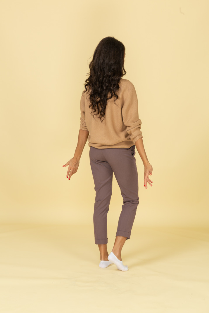 Three-quarter back view of a lost dark-skinned young female outspreading her hands