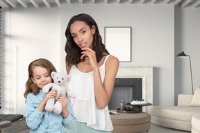 A mother and daughter holding a teddy bear in a living room
