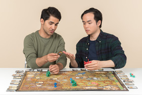 Two young interracial friends sitting at the table and playing board game