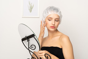 Mujer joven con gorra quirúrgica mirando su reflejo en el espejo