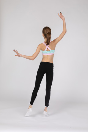 Back view of a teen girl in sportswear raising hands and putting her leg aside