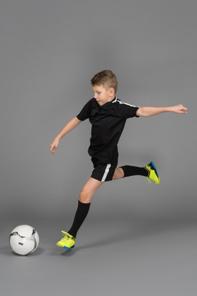 Vista di tre quarti di un ragazzino in uniforme di calcio che calcia un pallone