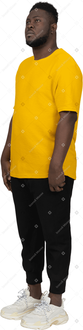 Vista di tre quarti di un giovane uomo dalla pelle scura con una maglietta gialla in piedi immobile