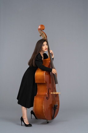 Vista lateral de una joven músico en vestido negro tocando su contrabajo