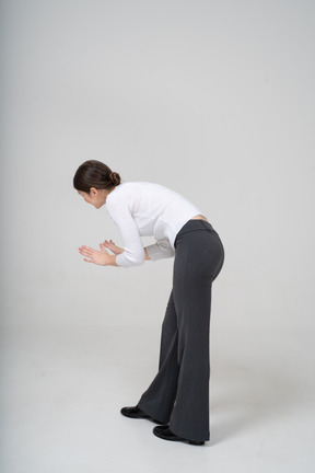 Side view of a woman in black pants and white blouse bending down