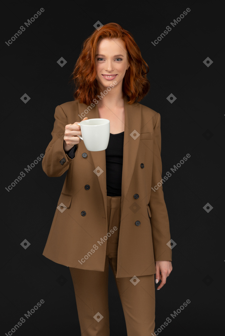 Smiling young woman in a brown suit holding out a cup