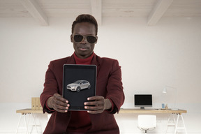 A man holding up a tablet with a car on it