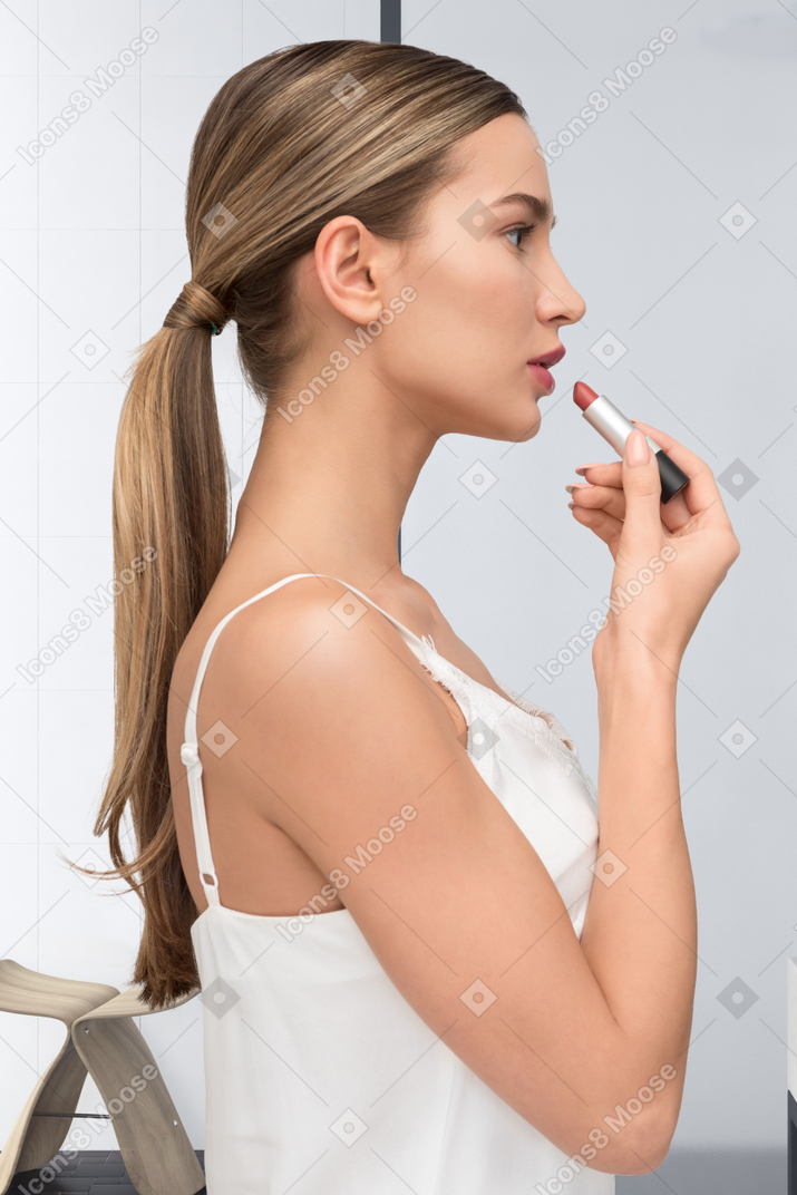 Young woman in white top applying red lipstick