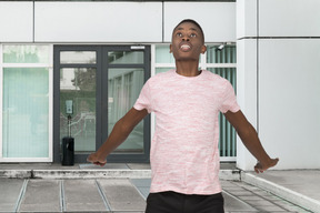 A young man with his arms outstretched in front of a building