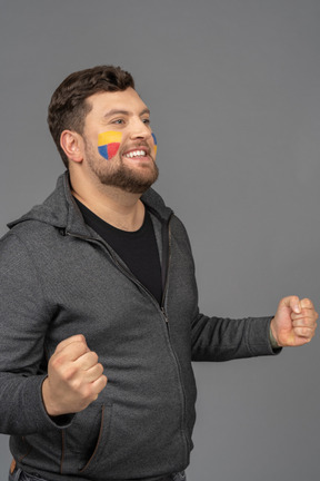 Three-quarter view of a satisfied male football fan with colorful face art clenching fists