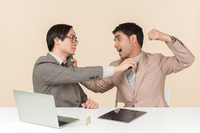 Two young nerds sitting at the table and punching each other into the face