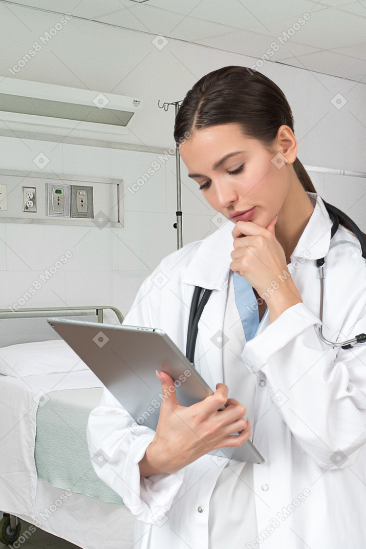 Woman doctor looking at information on tablet and thinking