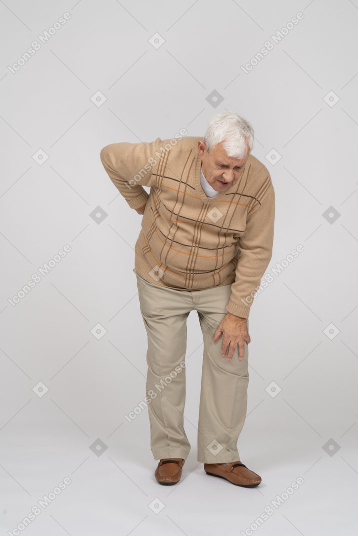 Front view of an old man in casual clothes bending down and touching his hurting knee
