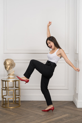 Вид сбоку счастливой молодой женщины, танцующей у золотой греческой скульптуры