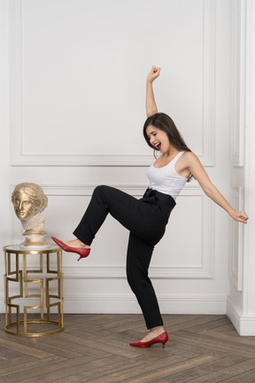 Side view of a happy young female dancing by a golden greek sculpture