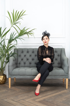A woman in black outfit sitting on a couch next to a potted plant