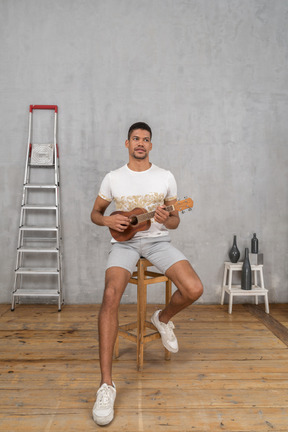 Vista frontale di un uomo su uno sgabello che suona l'ukulele