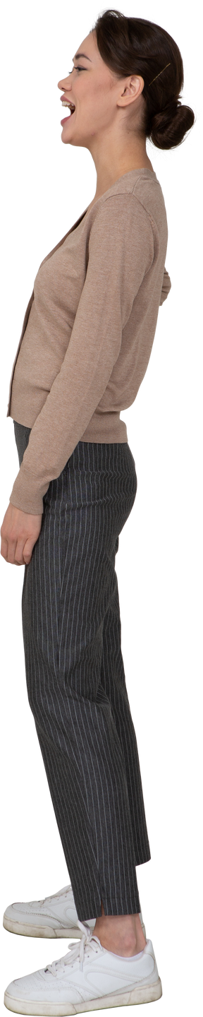 Vista laterale di una donna che ride in pullover e pantaloni mettendo la mano sul fianco