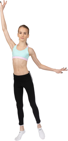 Front view of a teen girl in sportswear raising hands and putting her leg aside